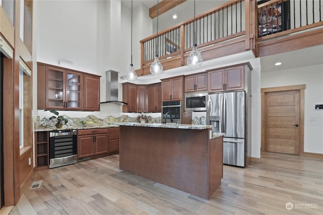 kitchen with hanging light fixtures, a towering ceiling, stainless steel appliances, beverage cooler, and wall chimney exhaust hood