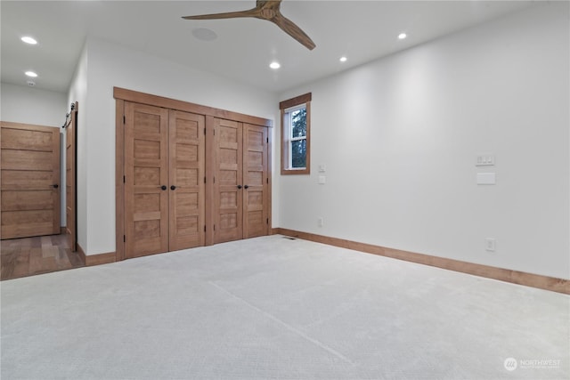 unfurnished bedroom with a barn door, ceiling fan, and carpet