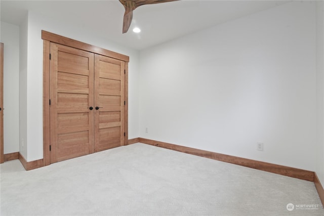 unfurnished bedroom featuring light carpet, a closet, and ceiling fan