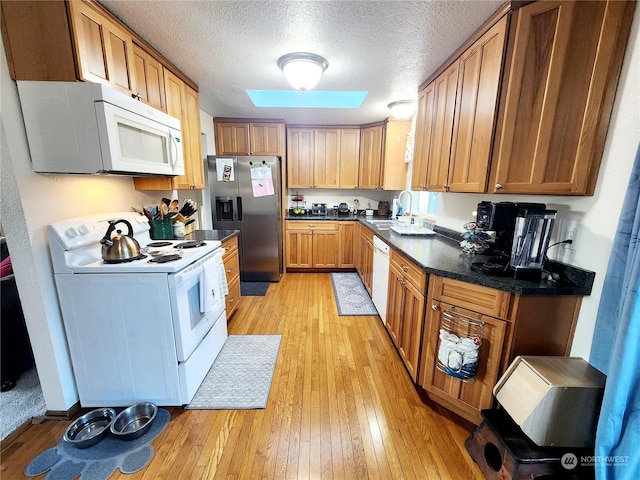 kitchen with white appliances, sink, a skylight, light wood-type flooring, and a textured ceiling