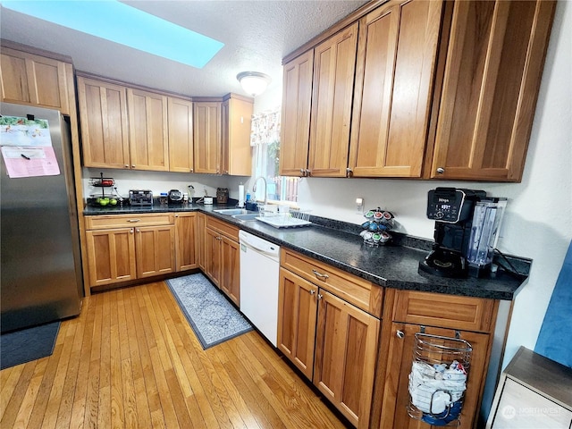 kitchen with white dishwasher, sink, light hardwood / wood-style flooring, a skylight, and stainless steel refrigerator