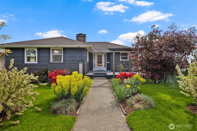 ranch-style home with a shingled roof, a wooden deck, a front yard, and a chimney