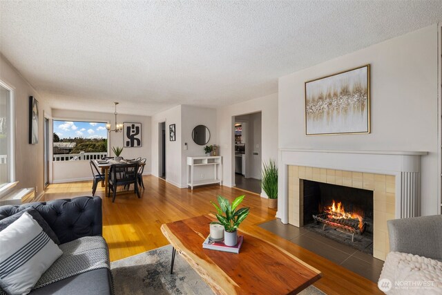 living area with an inviting chandelier, a tile fireplace, a textured ceiling, and wood finished floors