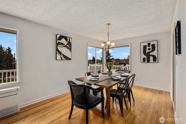 dining space featuring baseboards, light wood-style flooring, a textured ceiling, and a notable chandelier