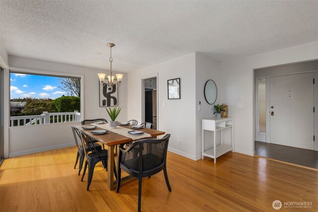 dining space with a textured ceiling, a notable chandelier, baseboards, and light wood-style floors