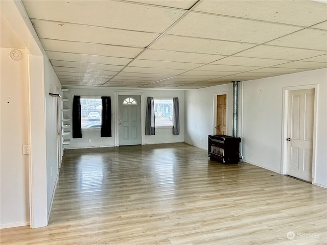 unfurnished living room with a paneled ceiling, light wood-type flooring, and a wood stove