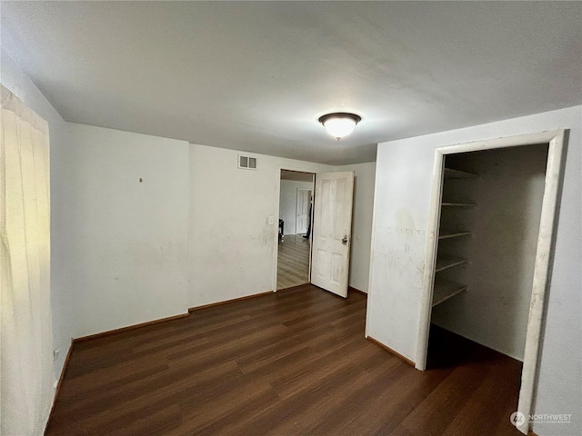 unfurnished bedroom featuring a walk in closet, a closet, and dark hardwood / wood-style flooring