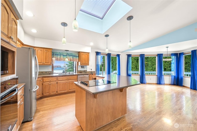 kitchen with a skylight, light hardwood / wood-style floors, decorative light fixtures, a kitchen island, and appliances with stainless steel finishes