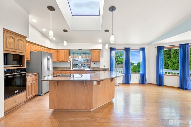 kitchen featuring black appliances, vaulted ceiling with skylight, light wood-type flooring, decorative light fixtures, and a kitchen island