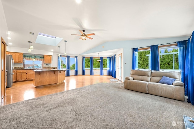 unfurnished living room featuring sink, light hardwood / wood-style flooring, ceiling fan, and vaulted ceiling with skylight