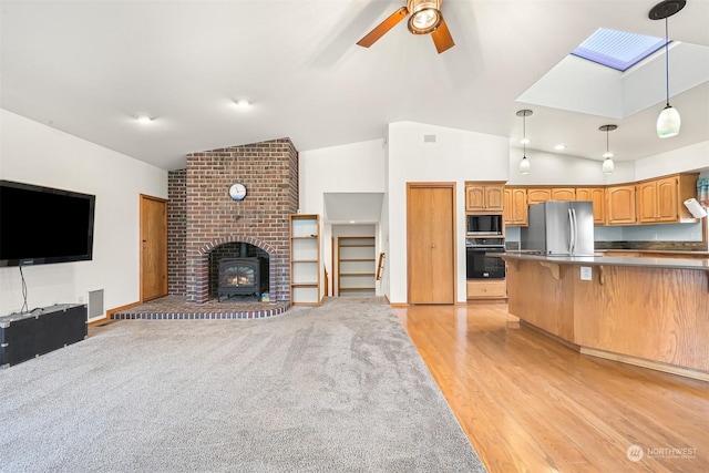 kitchen with pendant lighting, a wood stove, light hardwood / wood-style flooring, ceiling fan, and appliances with stainless steel finishes