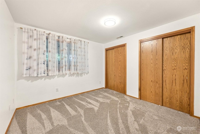 unfurnished bedroom with carpet floors and two closets