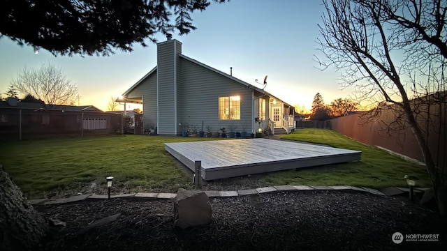 back house at dusk featuring a deck and a lawn