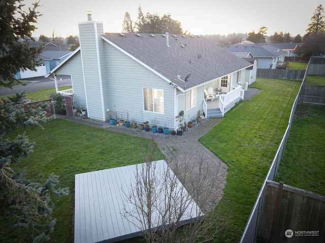 rear view of property featuring a shingled roof, a fenced backyard, a yard, and a chimney