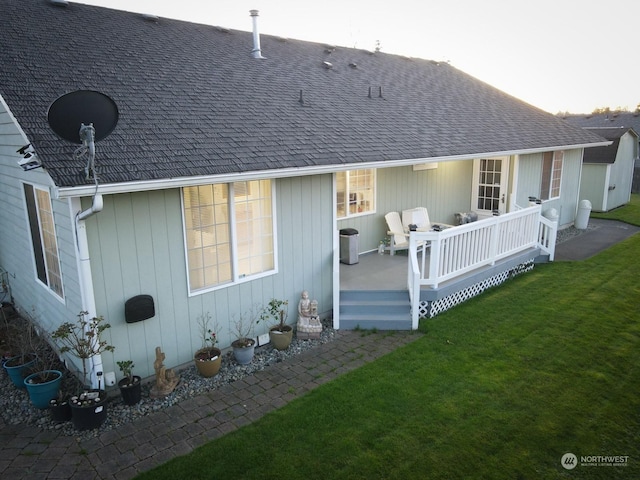 rear view of property with roof with shingles, a yard, and a deck