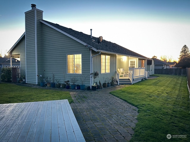 back house at dusk featuring a deck and a lawn