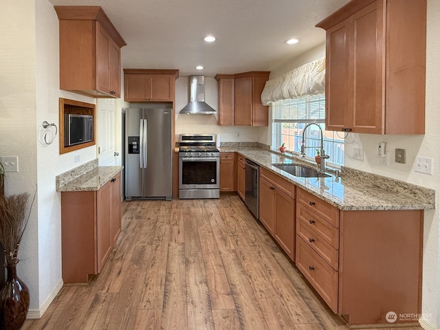 kitchen with light stone countertops, appliances with stainless steel finishes, light wood-type flooring, sink, and wall chimney range hood