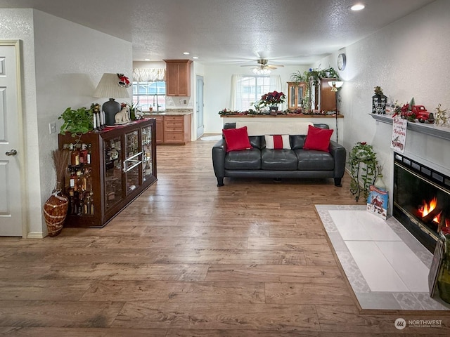 living room with a textured ceiling, light wood-type flooring, and ceiling fan