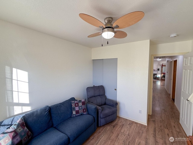 living area with ceiling fan, a textured ceiling, baseboards, and wood finished floors