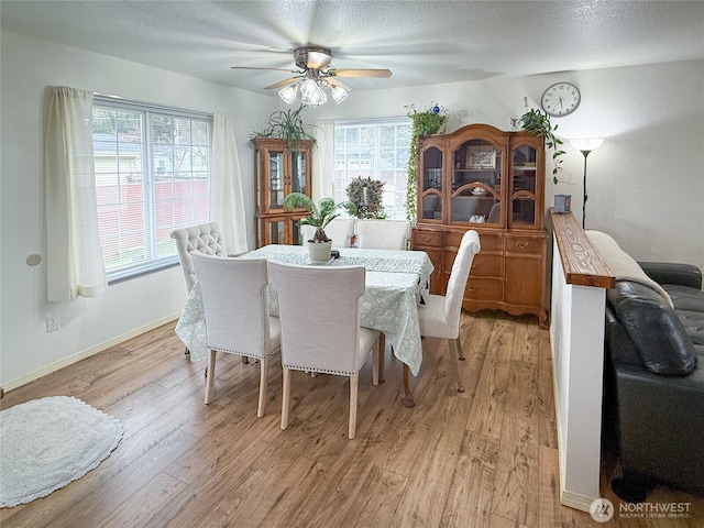 dining room featuring light wood-type flooring, ceiling fan, baseboards, and a textured ceiling