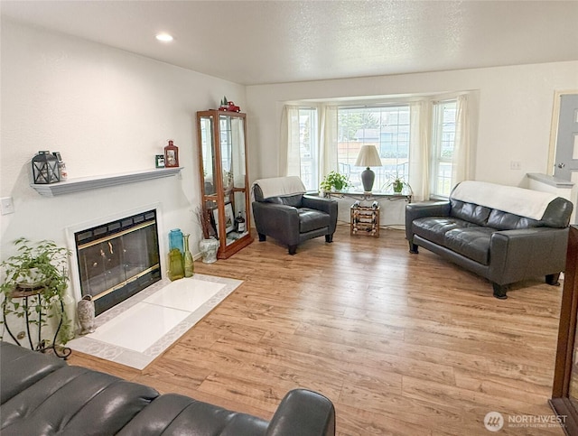 living room with recessed lighting, a fireplace with flush hearth, and light wood-style floors