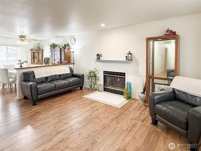 living area with a textured ceiling, a fireplace with flush hearth, light wood-style flooring, and a ceiling fan