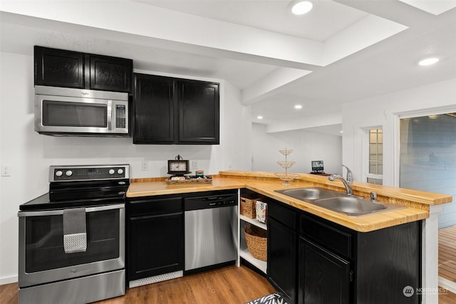 kitchen with appliances with stainless steel finishes, light wood-type flooring, sink, and kitchen peninsula