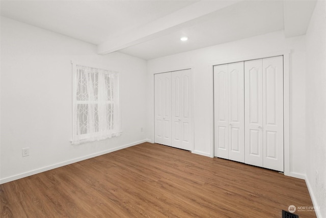 unfurnished bedroom with wood-type flooring, two closets, and beamed ceiling