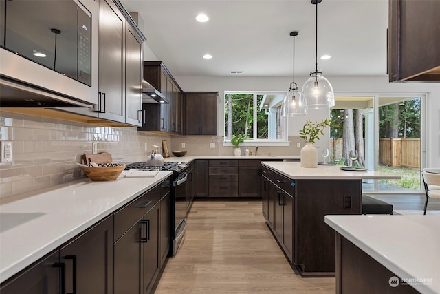 kitchen with ventilation hood, hanging light fixtures, dark brown cabinets, light hardwood / wood-style floors, and stainless steel appliances