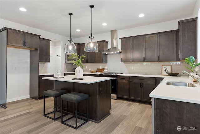 kitchen with electric stove, sink, hanging light fixtures, wall chimney exhaust hood, and light wood-type flooring