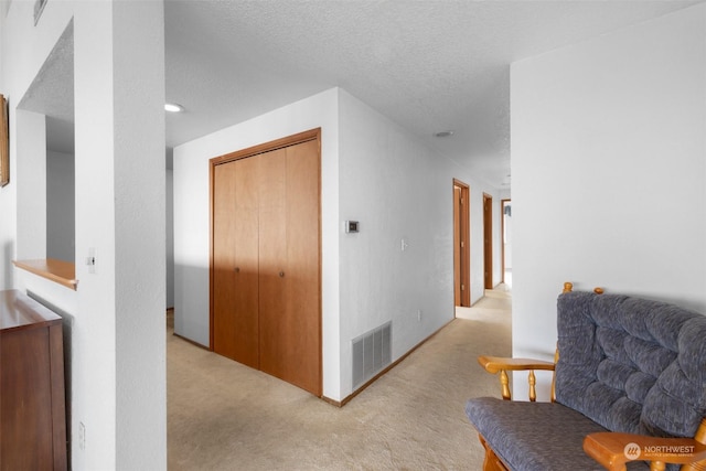 hall featuring light colored carpet and a textured ceiling