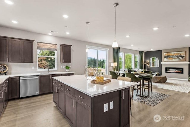 kitchen featuring light wood-type flooring, backsplash, sink, pendant lighting, and dishwasher