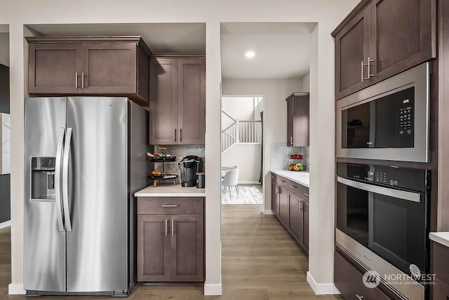 kitchen featuring tasteful backsplash, dark brown cabinetry, light wood-type flooring, and appliances with stainless steel finishes