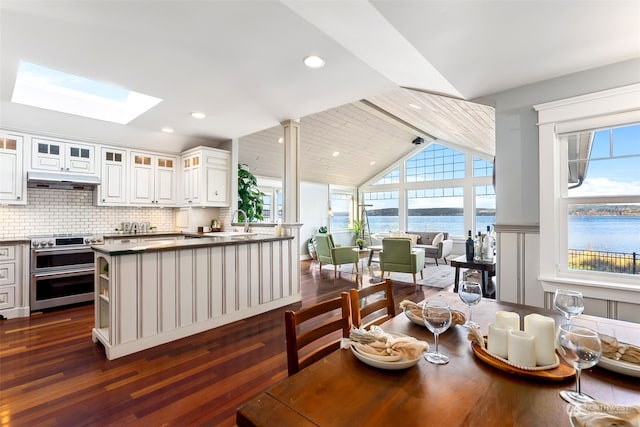 dining area with lofted ceiling with skylight, sink, a water view, and dark wood-type flooring