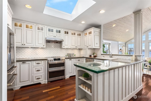 kitchen with dark hardwood / wood-style flooring, vaulted ceiling with skylight, high end appliances, sink, and white cabinetry