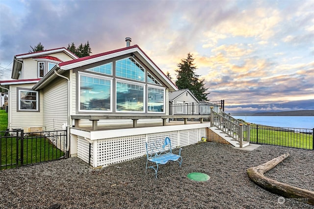 back house at dusk featuring a deck with water view and a lawn