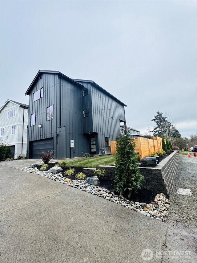 view of home's exterior with board and batten siding, an attached garage, driveway, and fence