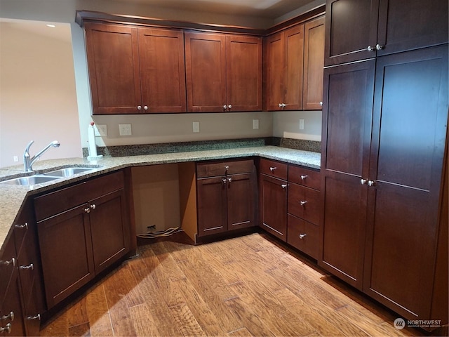 kitchen featuring kitchen peninsula, light hardwood / wood-style floors, light stone counters, and sink