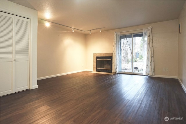 unfurnished living room with a fireplace, track lighting, and dark wood-type flooring