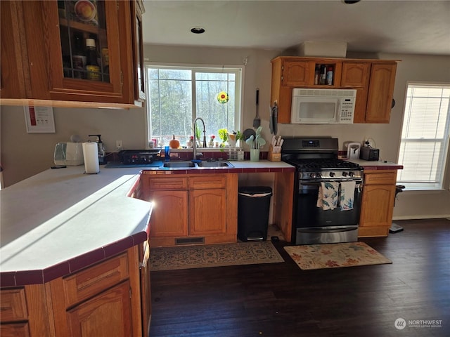 kitchen featuring stainless steel gas range oven, sink, dark wood-type flooring, and tile countertops