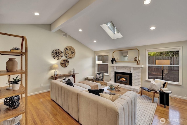 living room featuring a brick fireplace, light hardwood / wood-style flooring, and vaulted ceiling with skylight