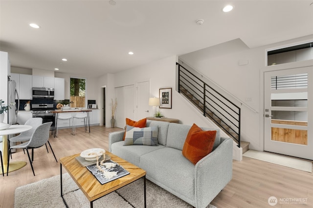 living room featuring recessed lighting, light wood-style flooring, and stairs