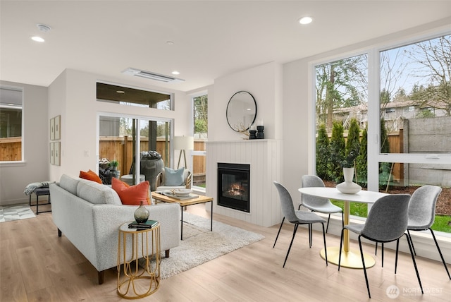 living area featuring a glass covered fireplace, recessed lighting, wood finished floors, and visible vents