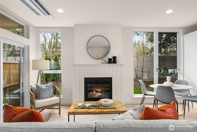 interior space featuring recessed lighting, plenty of natural light, a glass covered fireplace, and wood finished floors