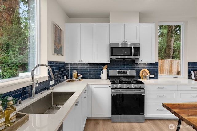 kitchen with a sink, white cabinetry, backsplash, and stainless steel appliances