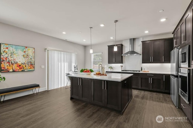 kitchen featuring dark hardwood / wood-style floors, a kitchen island with sink, decorative light fixtures, and wall chimney range hood