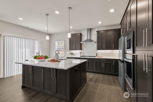 kitchen featuring a kitchen island with sink, sink, wall chimney range hood, pendant lighting, and dark hardwood / wood-style floors