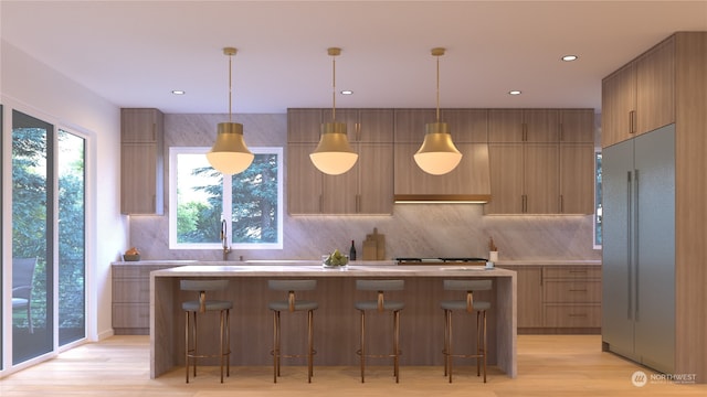 kitchen featuring pendant lighting, stainless steel built in fridge, light wood-type flooring, a wealth of natural light, and a kitchen island