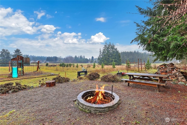 view of yard featuring a playground, a fire pit, and a rural view