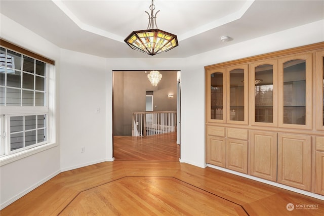 unfurnished dining area with a chandelier, a raised ceiling, and hardwood / wood-style flooring